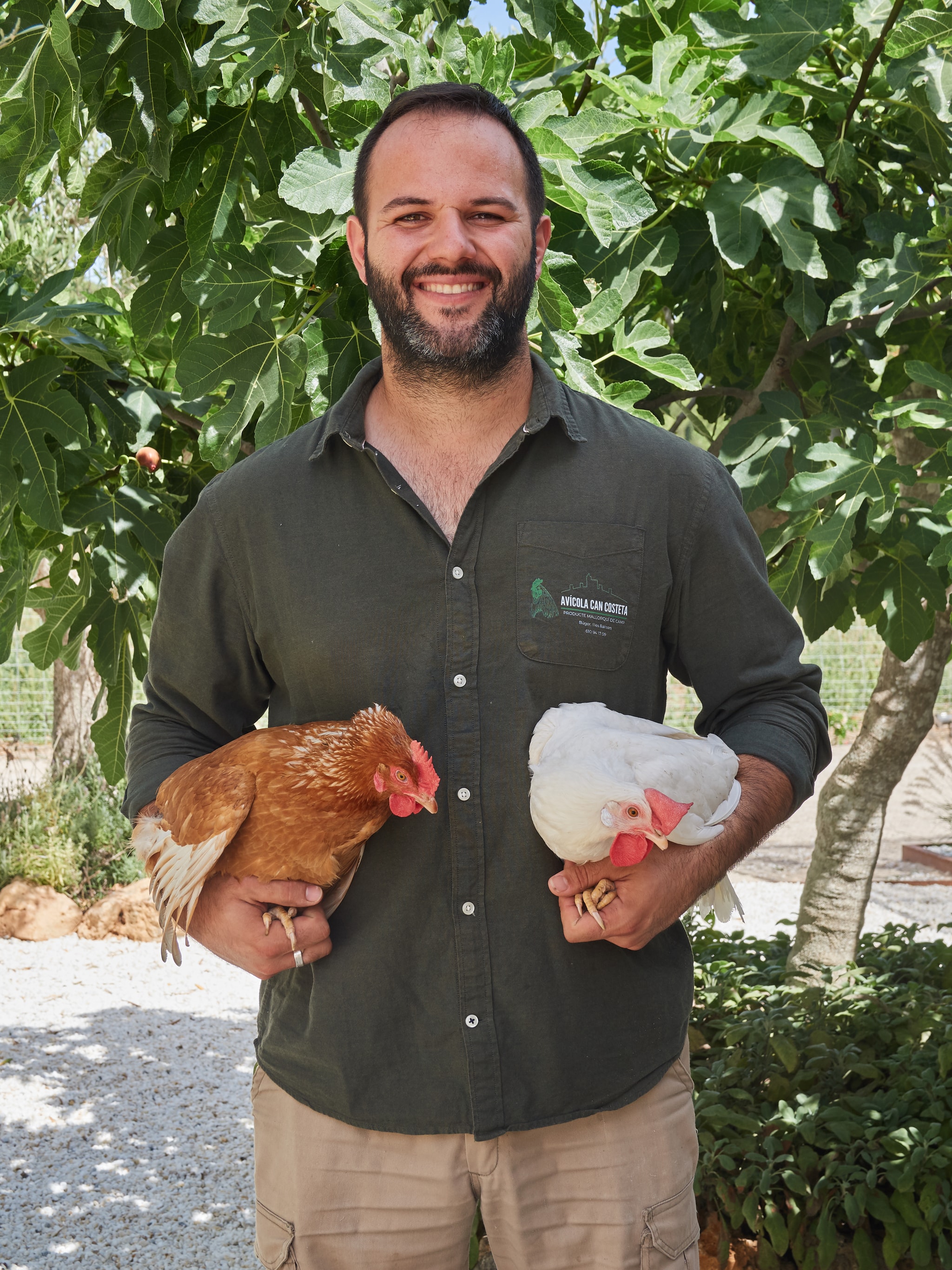 Un home de Can Costeta amb dues gallines als braços davant d'una figuera