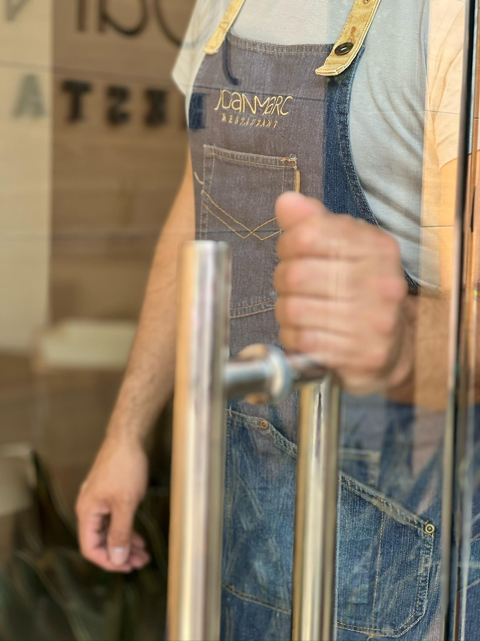 El davantal de Joan Marc i la mà a la maneta, a punt d'obrir la porta